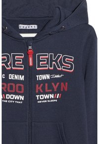 Felpa con zip di colore navy realizzata in tessuto morbido, con audaci grafiche testuali in bianco e rosso. Include un cappuccio con stringhe e tasche frontali.