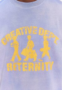 Lys blå bomull T-skjorte med en gul slitt trykk av tre figurer som går med poser og teksten "CREATIVE DEPT. RETERNITY."
