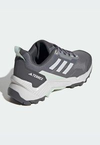 Pantofii sport gri cu dungi albe, superior din plasă texturată, talpă căptușită și accente verde deschis. Dispune de o talpă exterioară din cauciuc durabil.