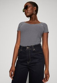 Top de manga corta a rayas en navy y blanco, combinado con jeans oscuros de cintura alta. La modelo lleva gafas de sol angulares y pendientes en forma de corazón.