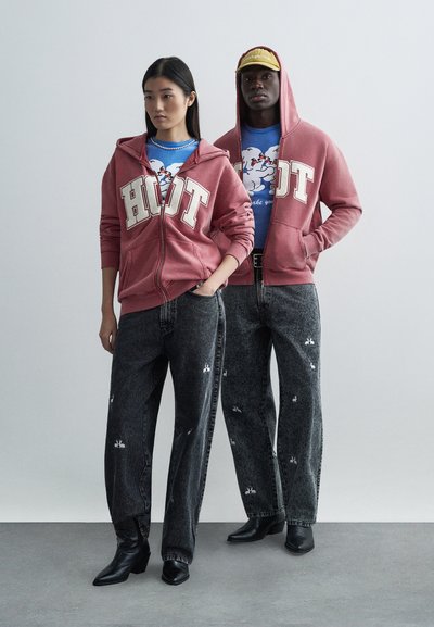 Red zip-up hoodie with "HOT" text, paired with blue graphic t-shirt. Dark denim jeans with bunny patterns and black pointed boots.