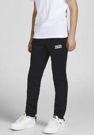 Pantalones jogger negros de algodón con un ajuste ceñido, que presentan el logo blanco "JACK & JONES" en el muslo izquierdo, combinados con zapatillas deportivas blancas.