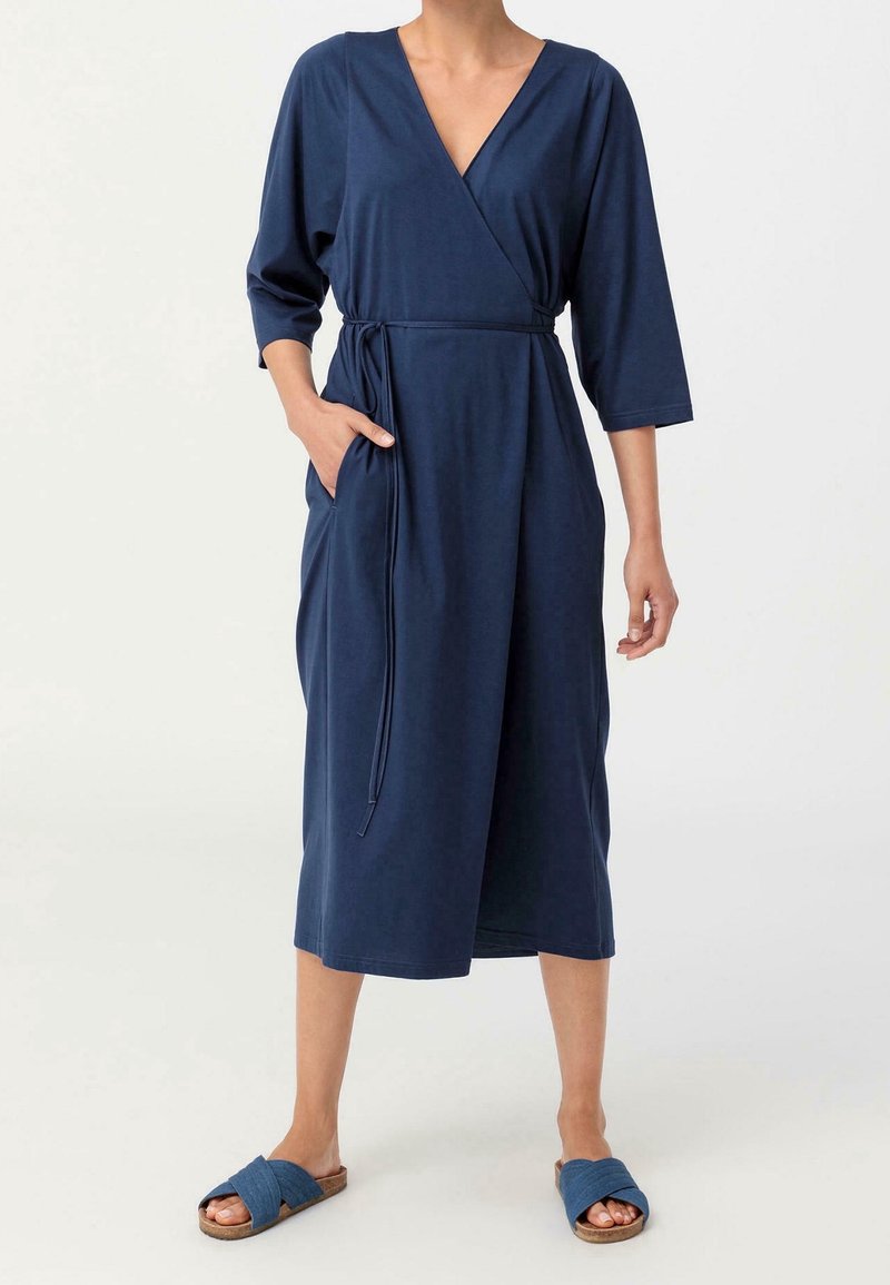 Robe portefeuille bleu marine en tissu doux, dotée de manches trois-quarts, d'une ceinture à la taille, de deux poches latérales et d'une longueur mi-mollet.