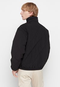Giacca invernale nera trapuntata con colletto alto, polsini ed orlo elasticizzati. Sul retro presenta una cucitura a motivo diamante e una vestibilità comoda.