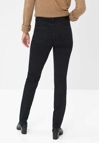 Jeans in denim nero con una vestibilità slim, dotati di due tasche posteriori e vita media. Indossati con un maglione beige e tacchi neri.