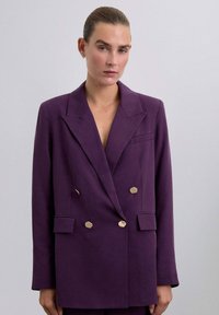Blazer doble faz de color púrpura con solapa, botones hexagonales dorados y un único bolsillo en el pecho, hecho de una tela suave.