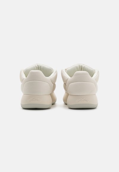Cream-colored sneakers with a smooth, matte upper, rounded heel, minimalistic design, and padded collar for comfort.
