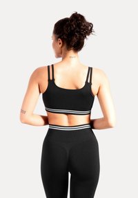 Sujetador deportivo negro con tirantes finos y rayas blancas en la parte inferior, combinado con leggings negros a juego que cuentan con una cintura alta y textura acanalada.