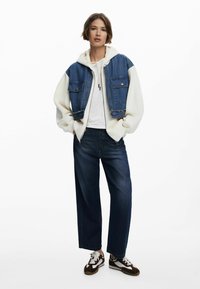 Denim jacket with white sleeves, two front pockets. Paired with a white hoodie, dark wide-leg jeans, and sneakers with brown and white accents.