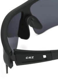 Schwarze Sonnenbrille mit dunklen Gläsern, umschließendem Design, matter Oberfläche und einem auf dem Bügel aufgedruckten Logo "CNZ". Sichtbare verstellbare Nasenpads.