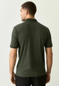 Polo de manga corta verde oscuro con un patrón de cuadros texturizados y un cuello clásico, con un ribete negro contrastante en las mangas.