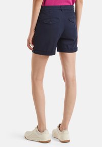 Námořnické modré bavlněné šortky s ohrnutými manžetami, se dvěma zadními kapsami na knoflíky, nošeny s bílými teniskami.