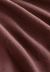 Tejido de punto en un color malva profundo con una textura suave, que presenta suaves ondas y sutiles variaciones en el grosor.