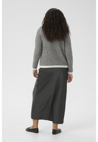 Pull en tricot à carreaux noirs et blancs à manches longues, associé à une jupe maxi fluide gris foncé et des chaussures plates noires.