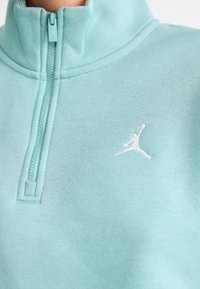 Svetlomodrá mikina na zips s vysokým golierom, so šedobielym logom Jordan. Hladká textúra a jednoduché švy.