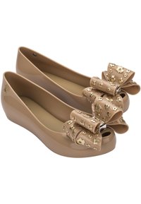 Ballerine in gomma beige con punta aperta, caratterizzate da un grande fiocco impreziosito da fiori dorati sul davanti. Texture liscia, tacco a zeppa.