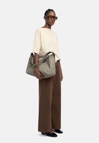 Szara torebka z zamszu o ustrukturyzowanym kształcie, dekorowana metalowymi ćwiekami wzdłuż boku, zestawiona z luźną kremową bluzką i szerokimi brązowymi spodniami.