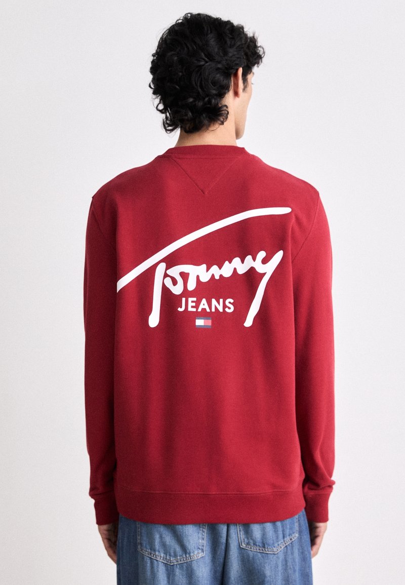 Sudadera roja con el logotipo blanco de "Tommy Jeans" en la parte posterior. Presenta un cuello redondo, puños de canalé y un diseño de corte relajado.