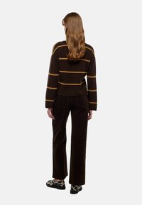 Pull en tricot marron avec des rayures jaunes, associé à un pantalon en velours côtelé marron et des chaussures à motifs noir et blanc. Design visible au dos.