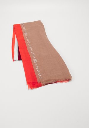 Foldet beige og rød Tommy Hilfiger tørklæde med frynser på kanterne og mærkenavnet trykt langs den beige stribe.