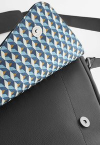 Black leather bag with a patterned flap in blue, cream, and orange geometric design. Features a metallic snap closure and fabric texture.
