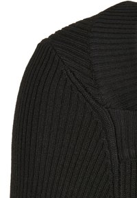 Pull en tricot côtelé noir avec un col épais et texturé, au design sans coutures, fabriqué dans un matériau doux et flexible avec des poignets allongés.