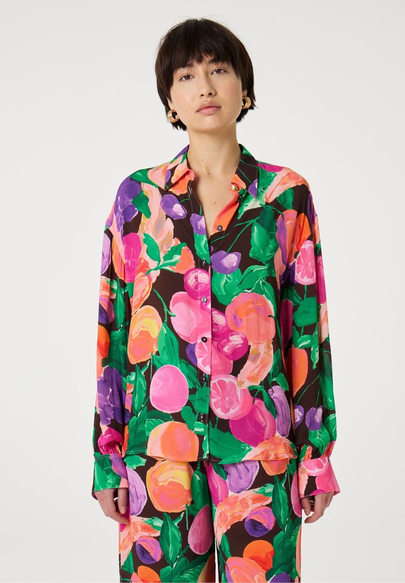 Bloes met bloemenmotief in multikleurige patronen met grote roze, oranje en paarse bloemen op een donkerbruine achtergrond. Lange mouwen, knoopsluiting aan de voorkant.
