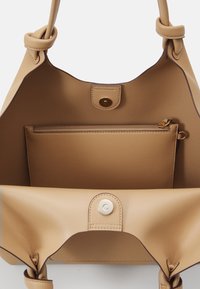 Beige skinnveske med et mykt, strukturert design. Har en knutehåndtak på toppen, magnetisk lukking og en glidelåslomme innvendig.