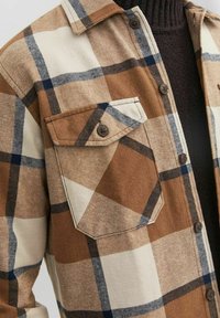 Bruine en crèmekleurige geruite overhemd met een knoopsluiting, voorzien van twee borstzakken, een stevige stoftextuur en contrasterende marineblauwe lijnen.