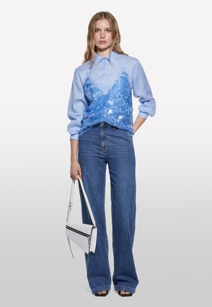 Chemise à manches longues bleu clair avec un superposé texturé en sequins et un col, associée à un pantalon large en denim bleu taille haute et un sac blanc.