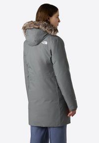 Grå udendørs parka med hætte kantet med faux pels, logo på venstre skulder, sidelommer og en glat, vandtæt overflade.