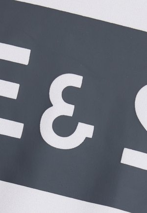 Gros plan sur un chiffre 3 blanc sur un fond rectangulaire gris foncé avec des caractères blancs adjacents partiels sur un tissu.