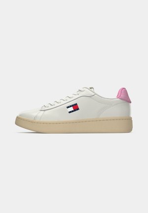 White low-top sneaker with beige sole, pink heel tab, white laces, and Tommy Jeans logo on outer side.