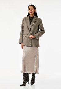 Lys grå struktureret blazer med dobbeltknapper, båret over en beige satin midi-nederdel, parret med sorte spidse hæle støvler.