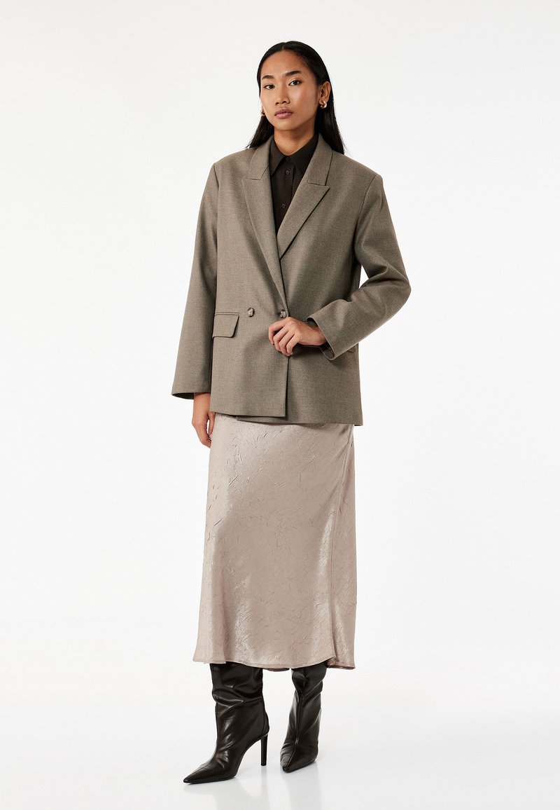 Ljusgrå strukturerad blazer med dubbla knappar, bärs över en beige satin midi-kjol, ihop med svarta spetsiga klackstövlar.