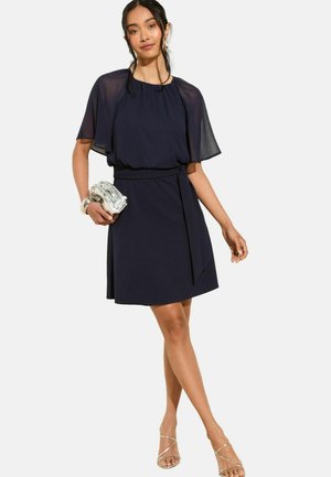 Marineblaues Kleid mit transparenten kurzen Ärmeln, taillierter Taille und ausgestelltem Rock. Inklusive einem passenden Gürtel und einem silbernen Clutch als Accessoire.