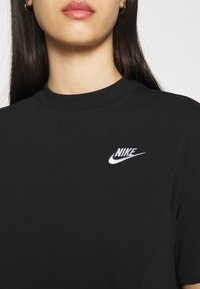 Black cotton t-shirt with a ribbed crew neck and a white embroidered Nike logo on the chest. The fabric appears smooth and fitted.