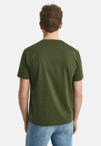 Tricou din bumbac de culoare verde măslin, cu mâneci scurte și guler rotund, având o croială lejeră și o textură netedă. Vedere din spate.