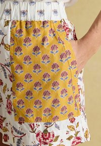 Cotton shorts featuring a yellow pocket with a floral pattern in shades of red and blue, combined with a white fabric adorned with similar florals.