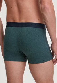Groene katoenen boxershorts met een marineblauwe elastische tailleband, die een gladde textuur en een aansluitend ontwerp tonen. Geen zichtbare patronen of afbeeldingen.
