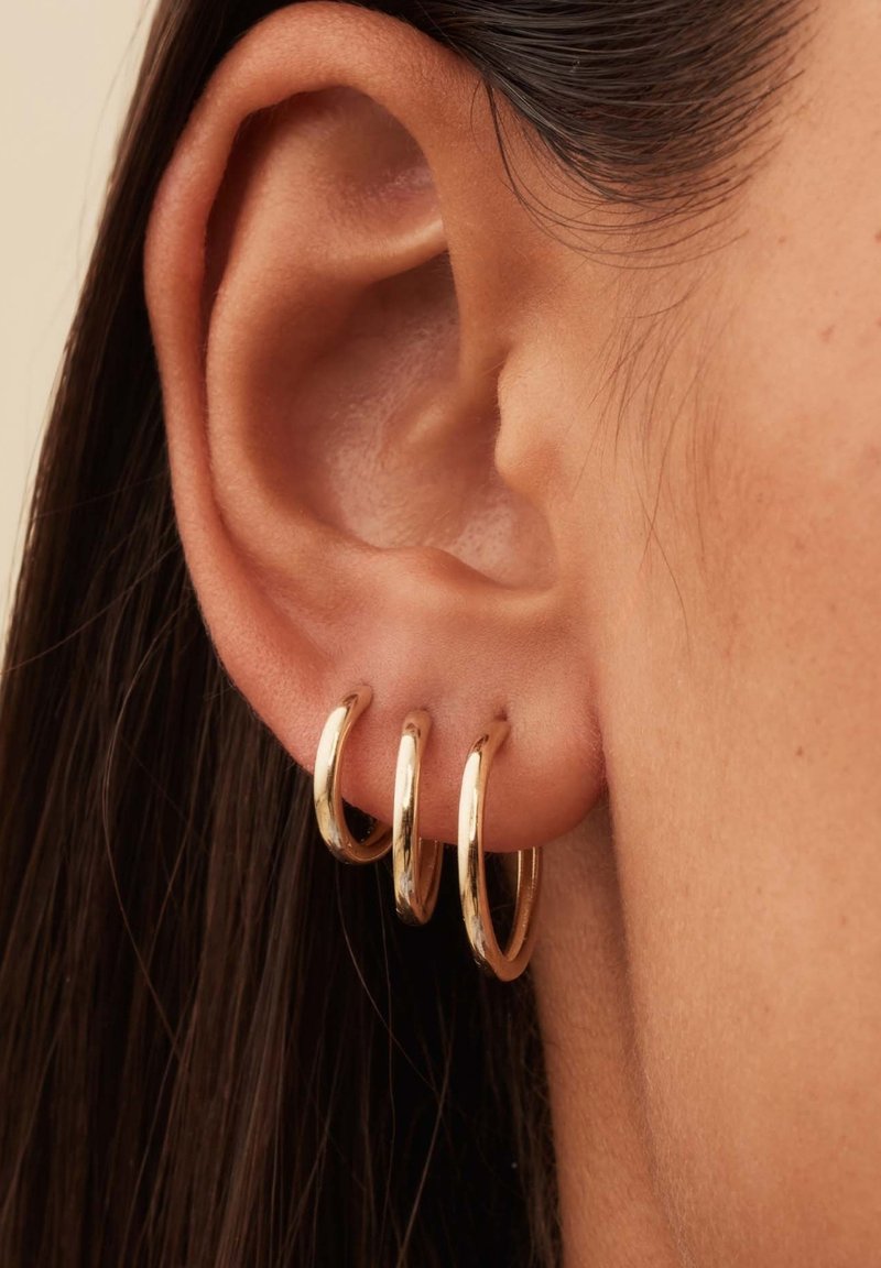 Des boucles d'oreilles créoles dorées en trois tailles portées à l'oreille. La surface est lisse avec une finition brillante, mettant en valeur leur design circulaire.