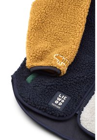 Fleece-innpakning med en sennepsgul topp og mørkeblå bunn, med tigermønster, teksturdetaljer og en merkevareetikett.
