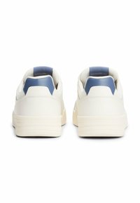 Zapatillas blancas con superficie de cuero suave, acentos en el talón azul acolchados y suela de goma texturizada. Diseño de corte bajo con costuras mínimas.