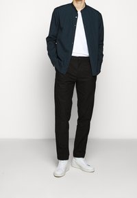 Granatowa koszula zapinana na guziki, biała koszulka pod spodem, czarne spodnie i białe trampki. Gładki materiał z luźnym krojem.