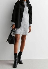Veste en denim noir, robe en tricot grise, bottines noires à talon et sac à main noir. Textures de tissu lisses et formes ajustées avec un design minimaliste.