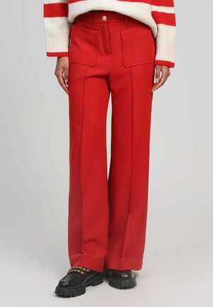 Personne portant un pantalon large rouge taille haute avec des poches plaquées à l'avant, associé à des mocassins noirs épais et un pull rayé blanc et rouge.