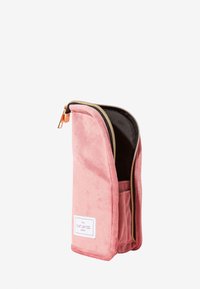 Rektangulær rosa fløyelspose med gullglidelås delvis åpen, svart innside og hvit etikett med teksten "THE FLAT LAY CO. LONDON."