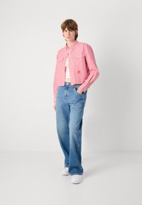 Röd- och vitrandig kort topp med långa ärmar, knäppt framtill, matchad med ljusblå, löst sittande jeans och vita sneakers.