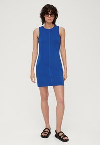 Blaues ärmelloses Kleid mit passgenauer Schnittführung, versehen mit einer Mittelnaht und einer glatten Textur. Kombiniert mit schwarzen klobigen Sandalen.