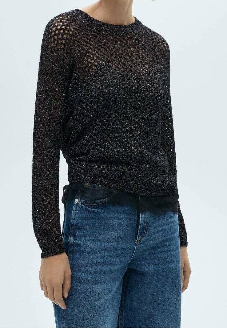 Zwarte gebreide trui met een open geweven ontwerp, lange mouwen en een geribbelde halslijn. Gecombineerd met blauwe spijkerbroeken.